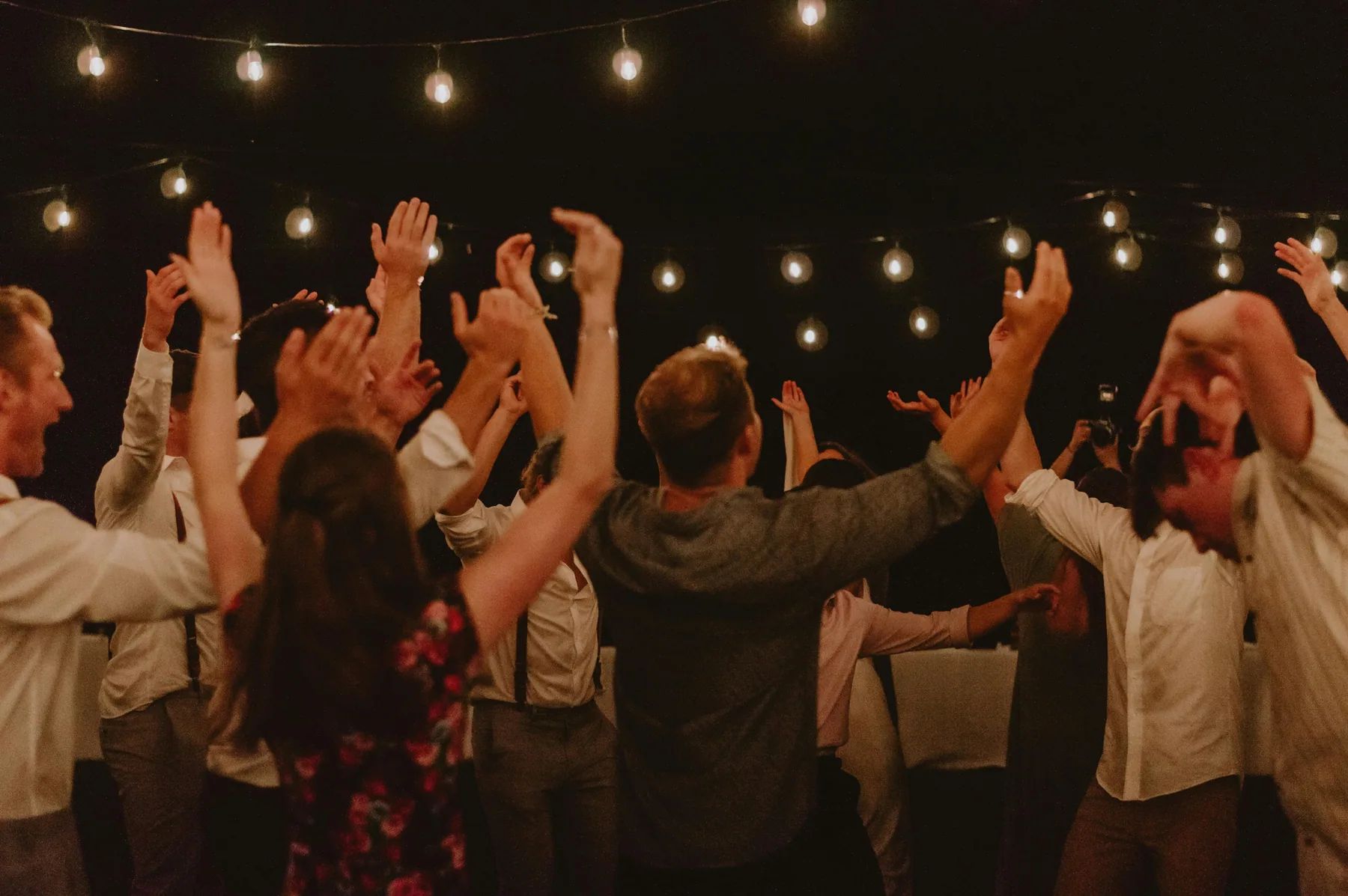 Invités les bras levés sur la piste de danse, sous des guirlandes lumineuses, pendant une soirée de mariage