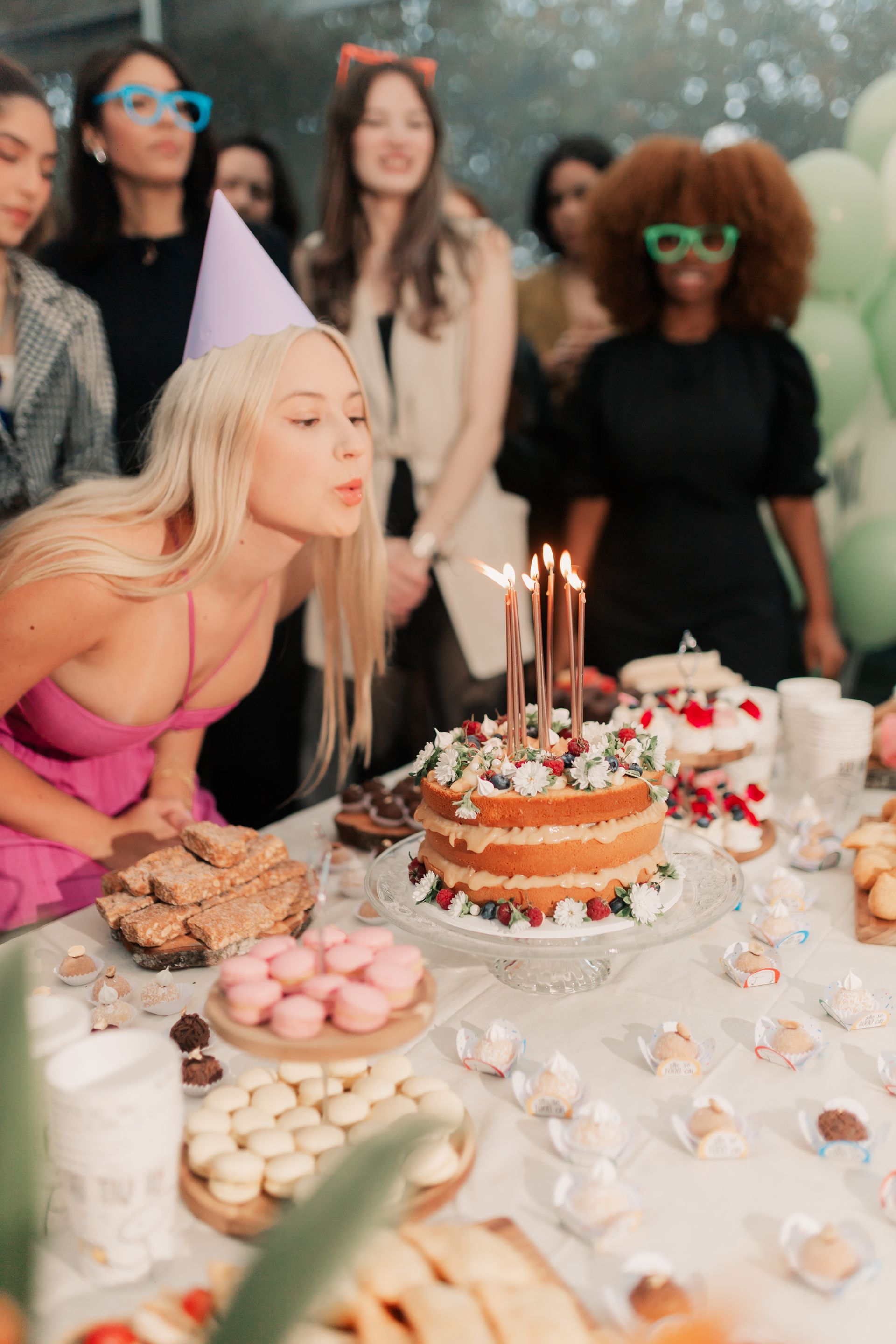 Femme soufflant les bougies de son gâteau d'anniversaire, entourée de ses amis