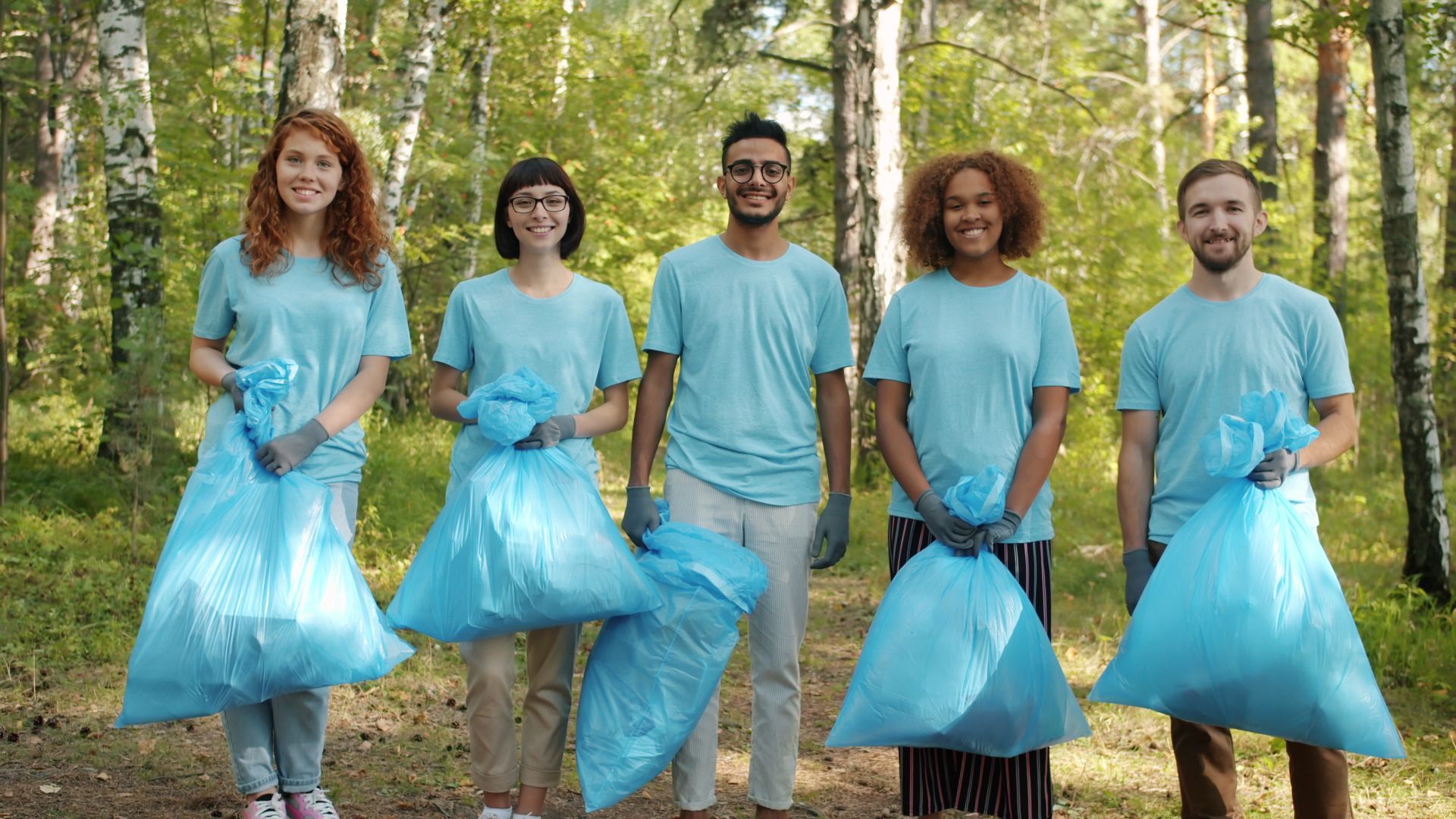 Groupe de bénévoles souriants en tenue assortie pendant une opération de nettoyage en forêt